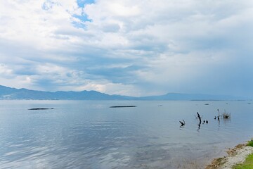 Naklejka premium Serene lake view with distant mountains and cloudy sky.