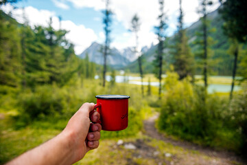 a red mug with tea or coffee in hand against a forest background