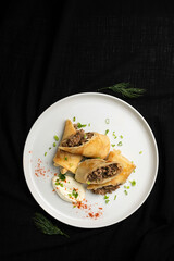 Stuffed Crepes with Mushroom Filling and Sour Cream on a White Plate.