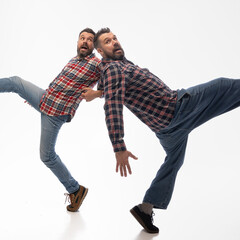 Two identical men gripping each other's arms, as if balancing or playfully stumbling in sync, with...