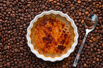 Coffee Creme Brulee  and Spoon Surrounded with Roasted Coffee Beans: Shallow ramekin of torched coffee creme brulee surrounded by whole coffee beans