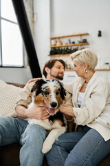 A couple sits together on a couch with their dog, sharing affectionate moments in their home.