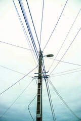 An electric pole with numerous stretched wires under a cloudy sky, creating a complex network of communication and power lines. Urban view of the infrastructure, where the wires go in different