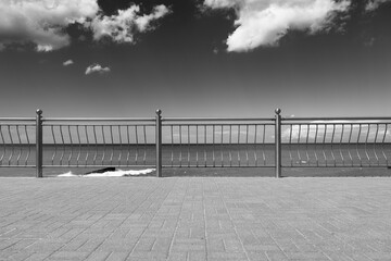 A classic black and white photograph capturing the serene beauty of a seaside promenade. The elegant railing, the calm sea, and the dramatic sky create a timeless image.