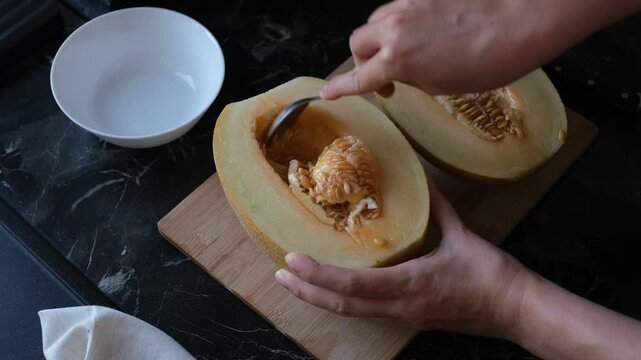 A young woman peels the seeds from a melon in her kitchen, close-up