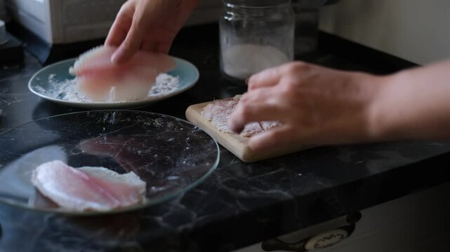 young woman dredges tilapia fish in flour before frying