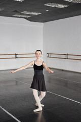 Obraz premium Vertical shot of smiling teenage girl wearing black dress for dancing getting ready to perform series of pirouettes while practicing ballet moves in dance studio with no people, copy space
