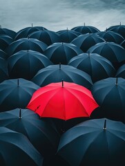 Obraz premium A single red umbrella stands out in a sea of black ones on a rainy day.