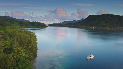 Aerial drone footage captures a serene sailboat anchored in the crystal-clear waters of Opunohu...