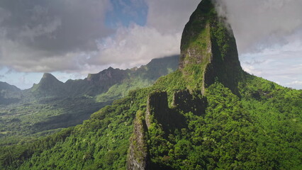 Breathtaking beauty of Moorea mountain landscape, covered by green forest hills and rugged stone ridge peaks against cloudy dramatic sky. Remote wild nature exotic travel background. Drone aerial shot