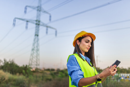 Female engineer using mobile phone inspecting power lines