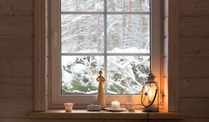 Scandinavian-style room in white wooden house, winter outside. Angel, candles, lantern on windowsill