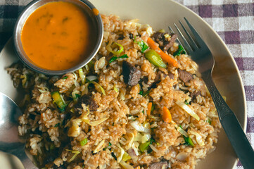 Close up to a plate of nepali buffalo fried rice called bhat bhuteko paired with spicy tomato sauce and served on a checkered tablecloth, authentic local daily staple food of Nepal