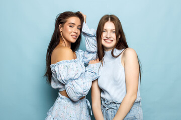 Two Friends Posing Together Against a Soft Blue Backdrop in Stylish Outfits During Daylight