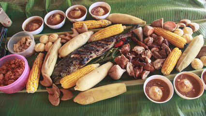 A traditional Filipino sharing meal called boodle fight featuring grilled fish, chicken, lechon, corn, and various vegetables arranged on banana leaves showing the authentic food of the Philippine 