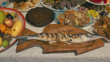 A table with a variety of authentic local Filipino dishes, featuring a grilled fish on a wooden board and assorted fruits for a traditional New Year eve feast or Media Noche in the Philippines