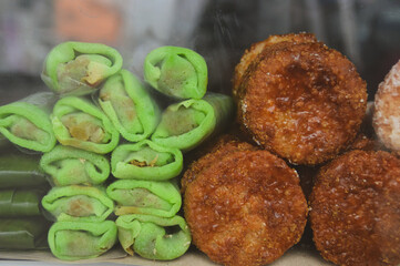 Green roll kue cucur and dadar gulung in a glass display, authentic local traditional Indonesian desserts popularly sold as street food