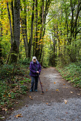 Obraz premium Senior woman with a walking stick getting fresh air on a gravel trail on a sunny fall day in the woods in Kirkland’s Watershed Park 