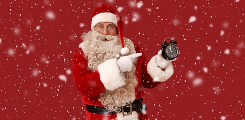 Shocked Santa Claus pointing at alarm clock on red background. Christmas countdown concept