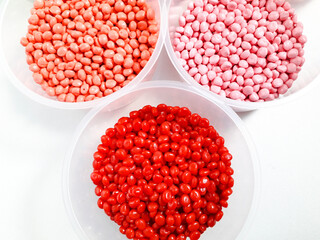 Pink, peach, and red masterbatch granules in a cup on a white background.Color pigment carrier polymers in the plastics industry