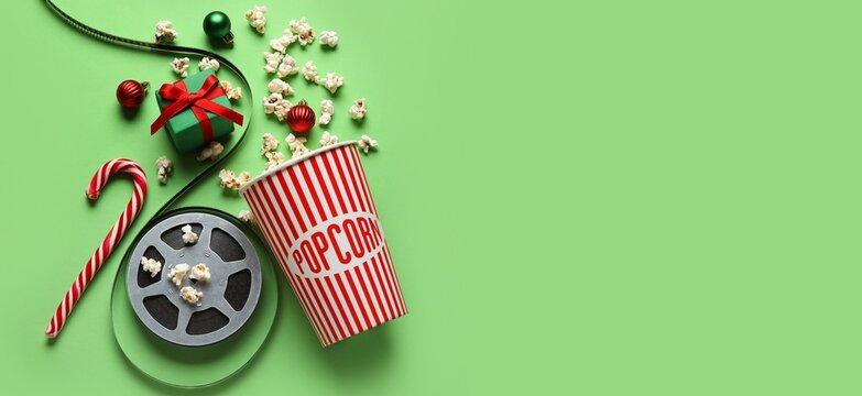 Bucket of popcorn, film reel, gift box and decorations on green background with space for text. Christmas movie concept