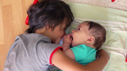 Young boy lying beside baby sibling, both lying on the floor in a calm moment of bonding, baby facing the boy, displaying affection and connection in a peaceful home environment