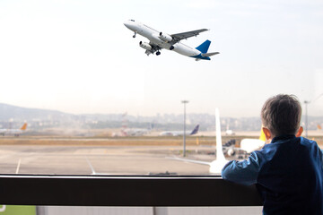 Kid watching planes taking off from airport window. Boy waiting for his flight. Aviation idea...