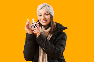 Young woman in winter clothes with snowflake on yellow background