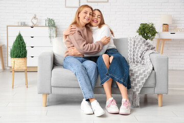 Happy young woman hugging her mother on sofa at home. International Hug Day