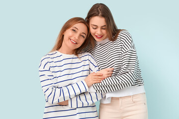 Beautiful young woman hugging her happy mother on blue background. International Hug Day