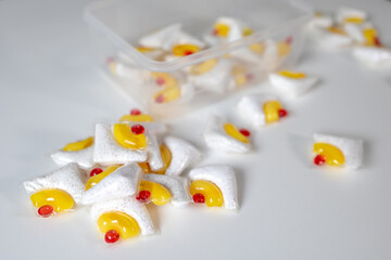 Dishwasher detergent tablets scattered on white surface, Cleaning pods with yellow liquid gel and...