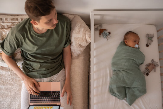 Father looking at sleeping newborn while working