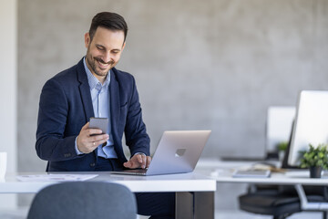Businessman Smiling While Using Smartphone at Work Desk