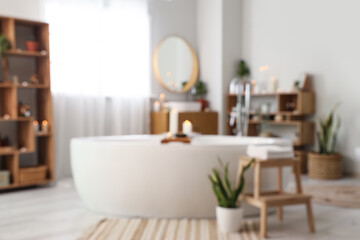 Blurred view of stylish bathroom with burning candles, bathtub and shelf units