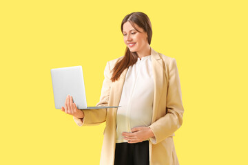 Young pregnant businesswoman with laptop on yellow background