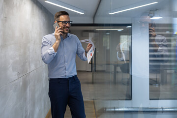 Businessman Talking on Phone While Holding Documents in Office