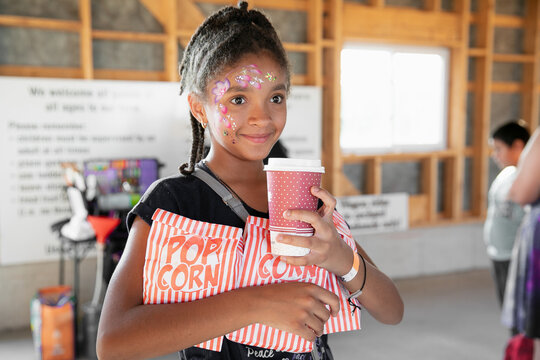 Tween girl holding armfuls of popcorn and a covered cup of cola