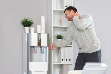 Young businessman suffering from neck pain near shelf in office