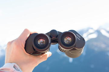 Hand holding binoculars with mountain view in background