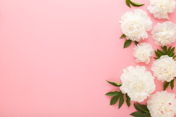 Fresh beautiful soft white peony flowers with green leaves on light pink table background. Pastel color. Closeup. Empty place for inspirational text, lovely quote or positive sayings. Top down view.
