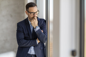 Contemplative Businessman Standing by Office Window in Thought