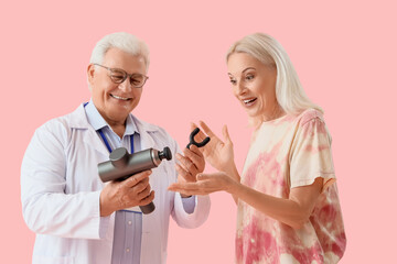 Male physiotherapist showing percussive massager to mature woman on pink background