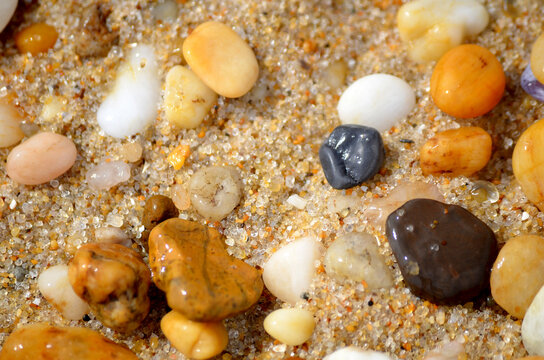 Lots of tumbled rocks on a sandy beach with water close up