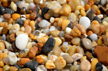 Lots of tumbled rocks on a sandy beach with water close up