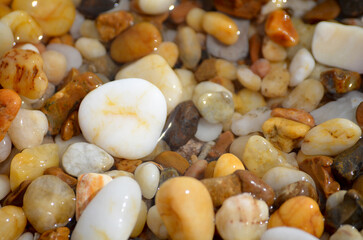 Lots of tumbled rocks on a sandy beach with water close up