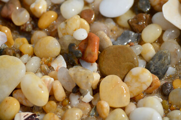 Lots of tumbled rocks on a sandy beach with water close up