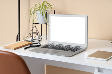 Fototapeta premium Modern table with laptop and houseplant near beige wall in room, closeup