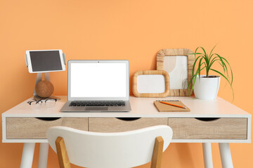 Fototapeta premium Stylish table with modern laptop and tablet near orange wall in room