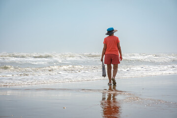 Woman walking in colorful clothes carrying a plastic bag next to the ocean