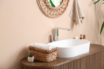 Modern sink and bath supplies on wooden chest of drawers near beige wall in bathroom